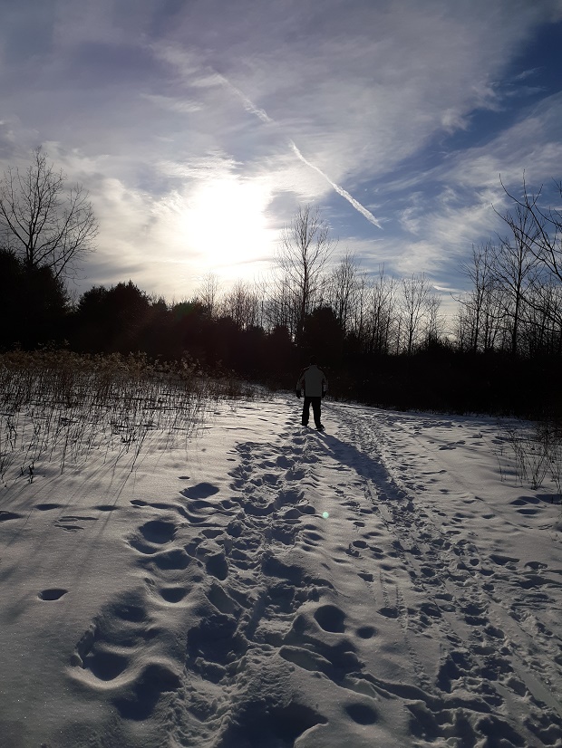 person snowshoeing in deep snow under sun and clouds
