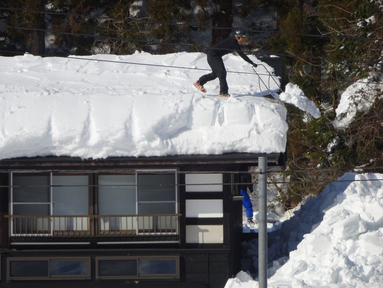 man on roof of house shoveling snow