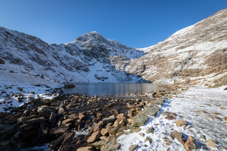 snow on mountains surrounding water with rocks in foreground