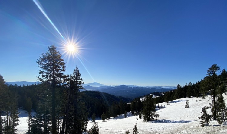 snow under blue sky with sun overhead and mountains in background