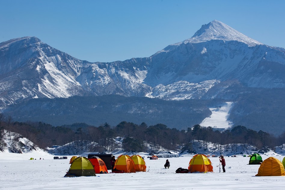 Urabandai winter activities: ice fishing tents on a frozen pond with mountains in the background