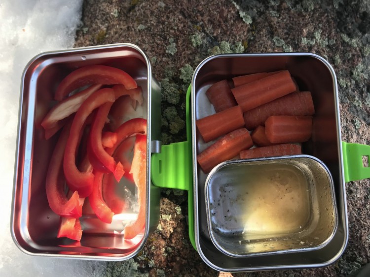peppers and carrots with salad dressing sitting on log in sustainable snack containers