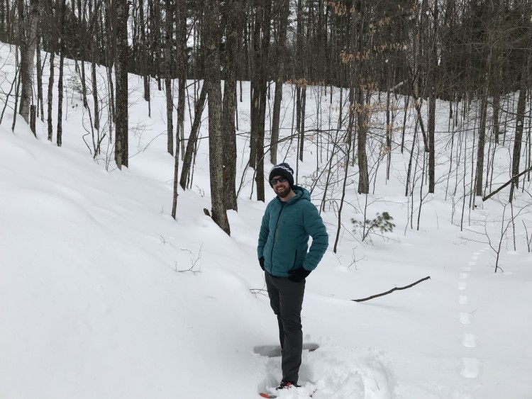 man on snowshoes with trees in background smiling in deep snow