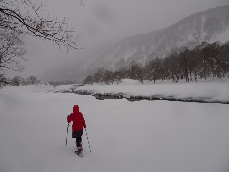 Yukiguni: person snowshoeing towards a snowy river with clouds above