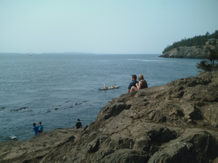 people sitting on rocky outcropping and watching ocean and kayakers