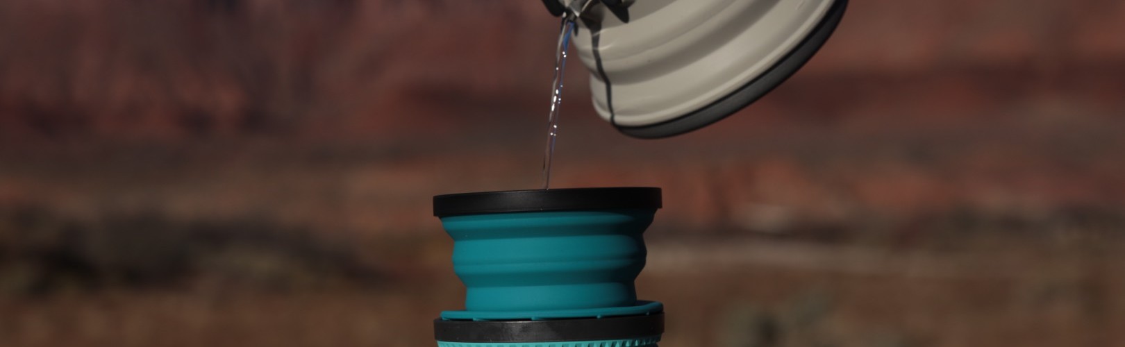 hand pouring tea kettle into mug on outdoor table