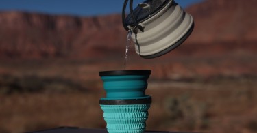 hand pouring tea kettle into mug on outdoor table