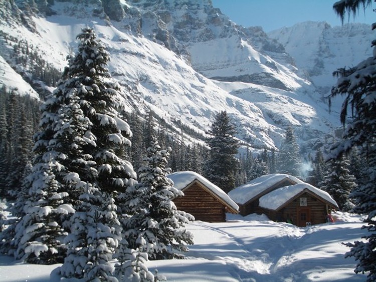 two cabins in snow with snow capped tress in foreground and mountains in background