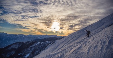 person snowshoeing down a steep mountain with sunset and other peaks in the background