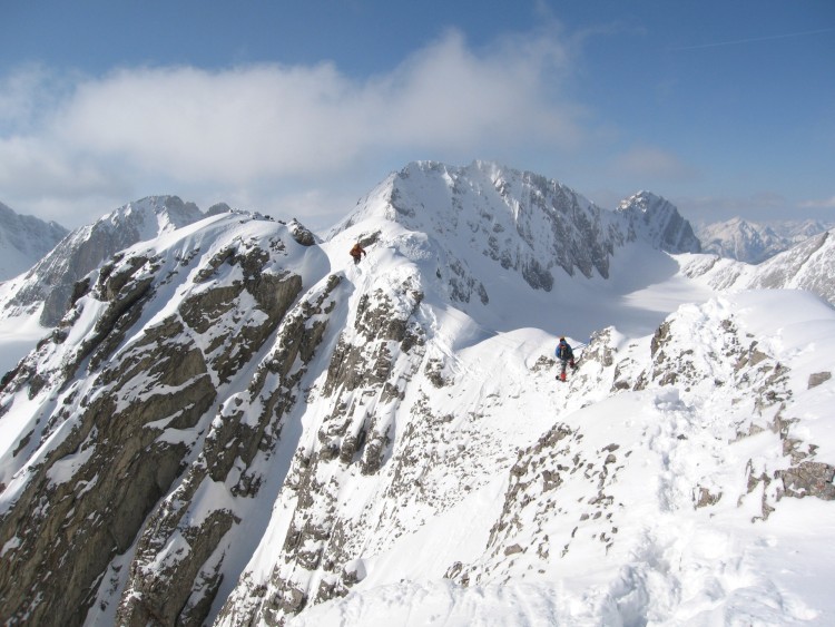 man sitting atop a tall mountain vista covered in snow