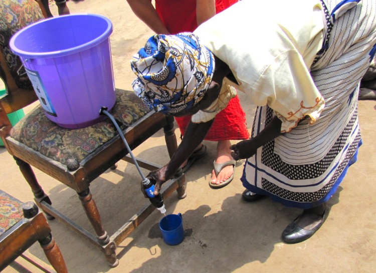 woman using Sawyer squeeze filter connected to bucket system