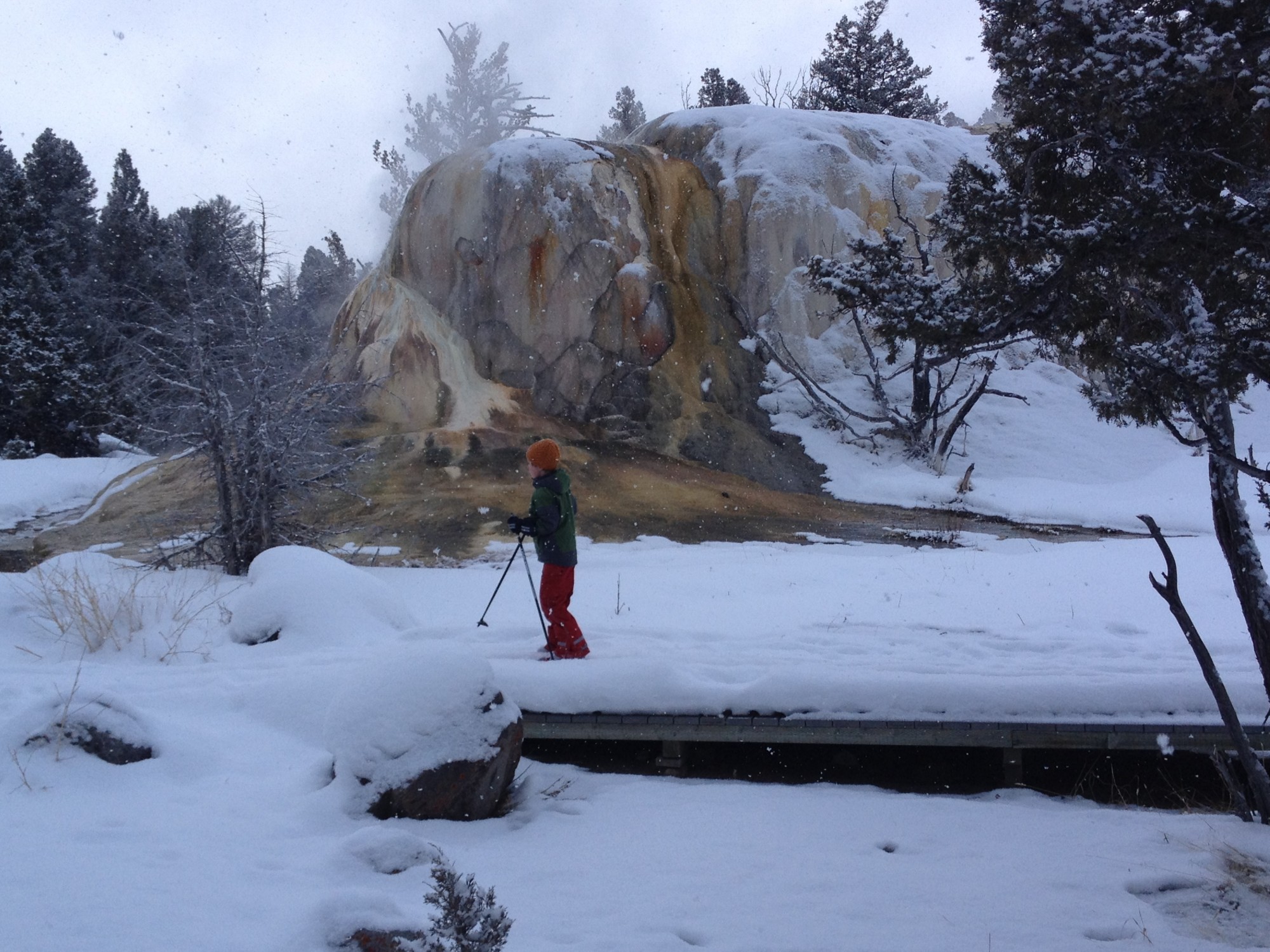 snowshoeing child in front of big, orange geyser mound