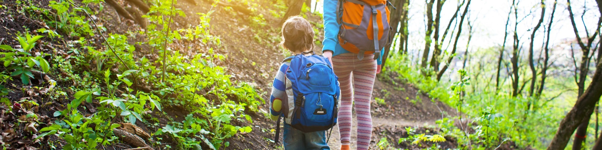 mom and child hiking on trail in forest with sun shining through trees