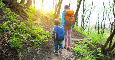 mom and child hiking on trail in forest with sun shining through trees