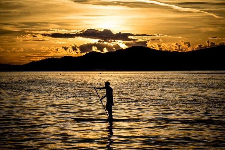 paddle boarder on water during sunset with mountains in background
