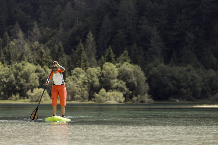 woman paddle boarding on a lake with trees in background