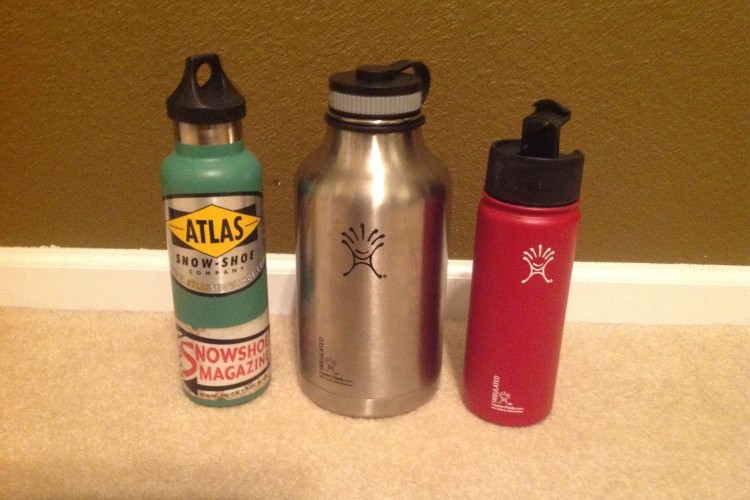 three Hydro Flask bottles sitting next to each other against a wall