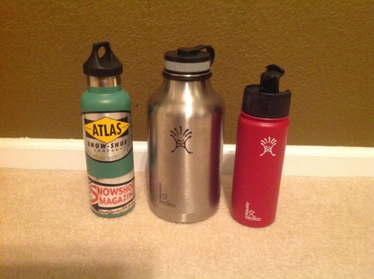three Hydro Flask bottles sitting next to each other against a wall
