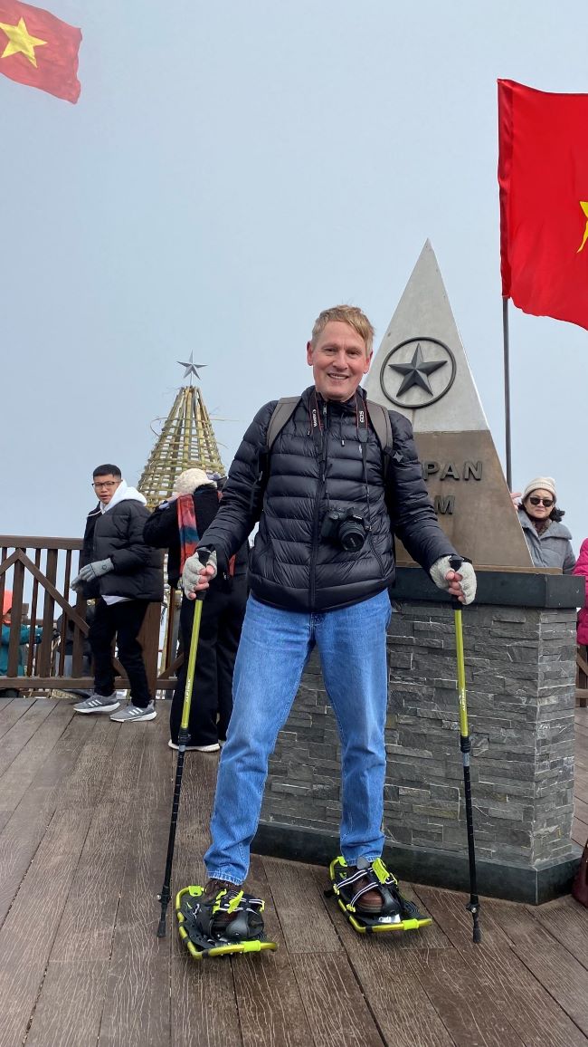 man with snowshoes on top of mountain near sign with people in the background