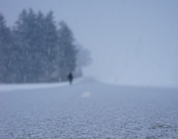 close up of snow on road with figure in background