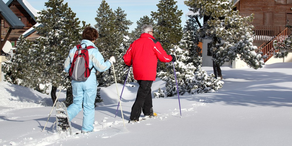 activities for arthritis: two seniors snowshoeing with trees and homes in background