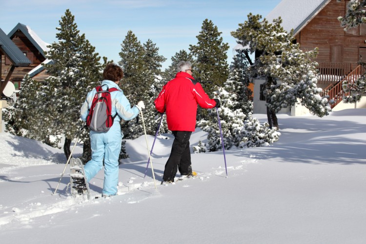 activities for arthritis: two seniors snowshoeing with trees and homes in background