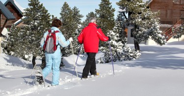 activities for arthritis: two seniors snowshoeing with trees and homes in background