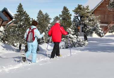 activities for arthritis: two seniors snowshoeing with trees and homes in background