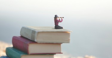 miniature woman on top of books with spyglass