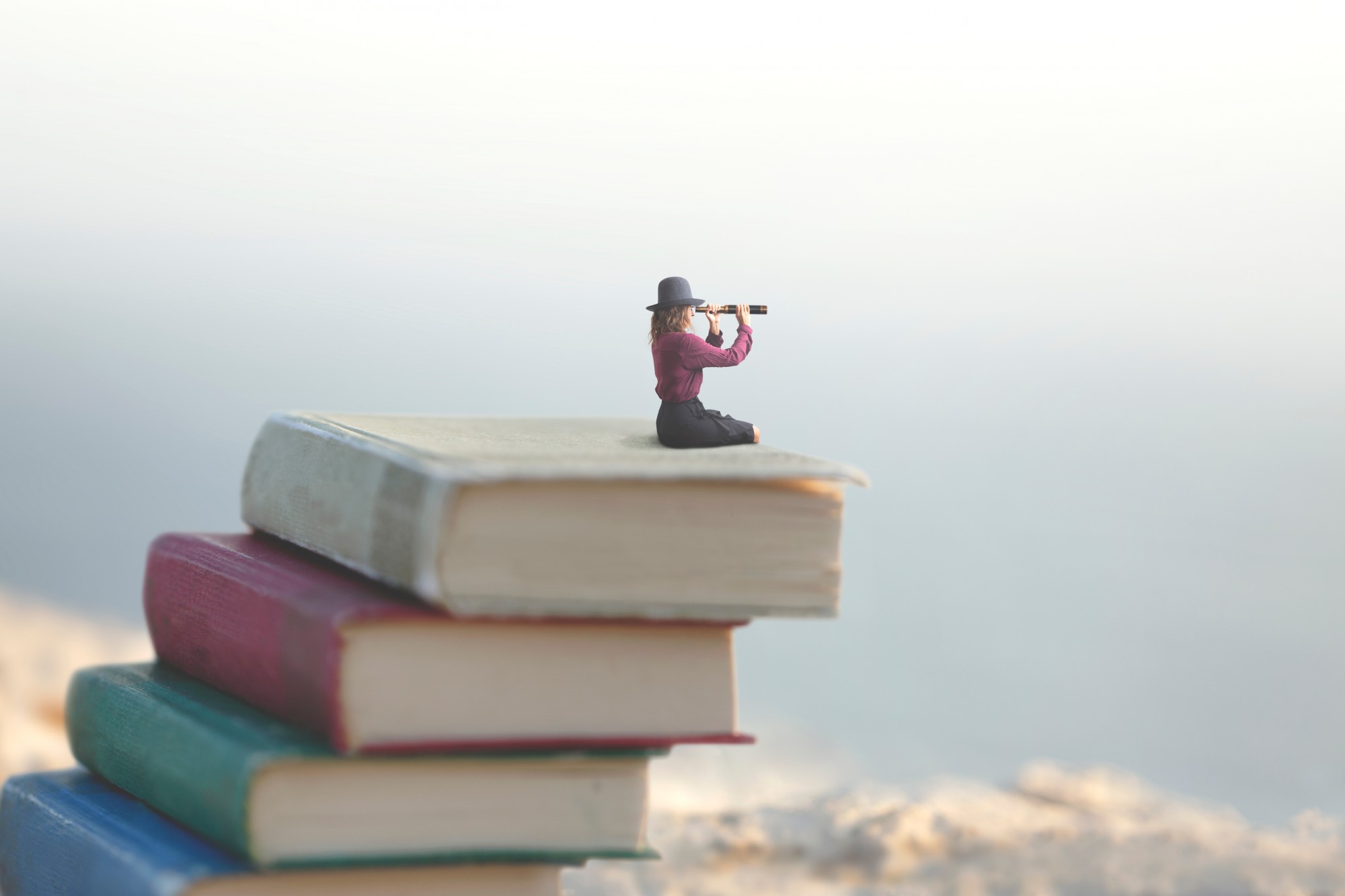 miniature woman on top of outdoor adventure books with spyglass