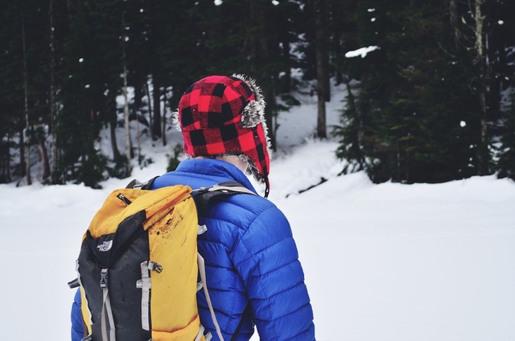 person in red hat, blue jacket and yellow backpack with snow in background