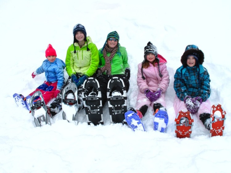woman and four kids sitting in the snow wearing snowshoes