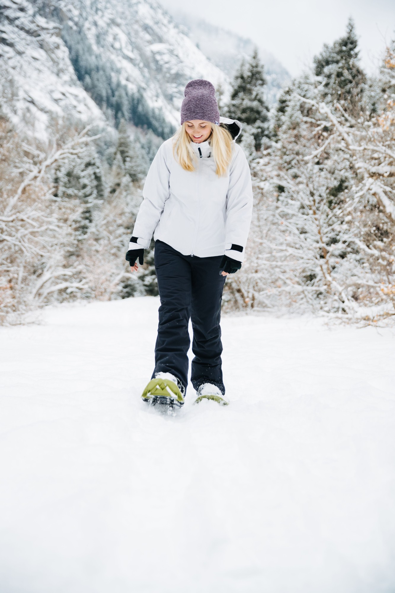 woman looking down and snowshoeing with trees in background