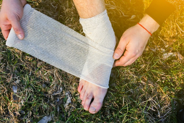 person wrapping sprained ankle while outdoors