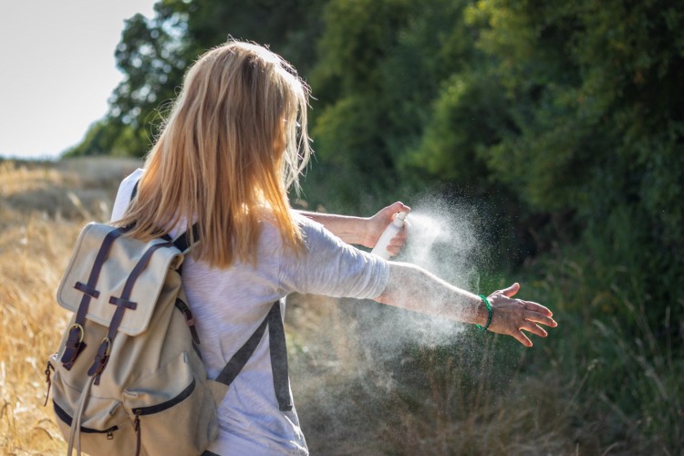 woman spraying mosquito repellant in outdoors
