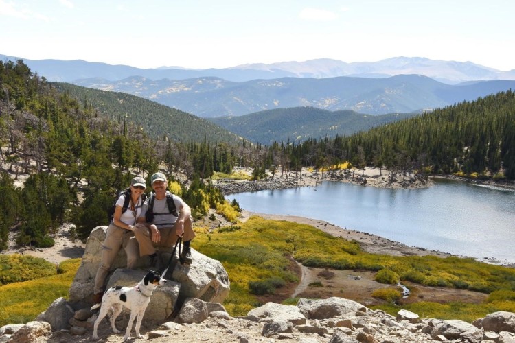 outdoor photo tips: couple and dog in front of water with open sky and mountains in background