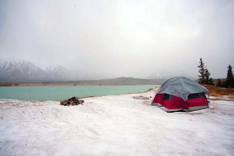 tent and logs near lake with clouds covering mountains