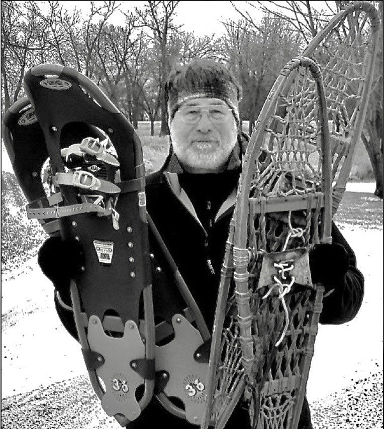 black and white photo of man holding one pair of modern and one pair of traditional snowshoes