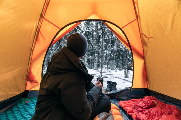 person looking out of tent in winter surrounded by sleeping bags