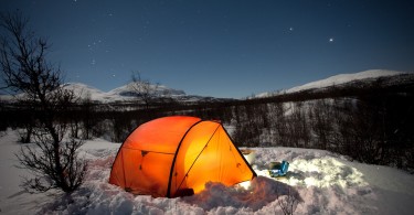 bright orange tent at night with snow on ground and clear starry sky above