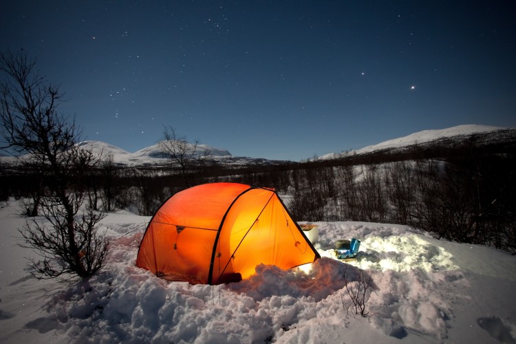 bright orange tent at night with snow on ground and clear starry sky above