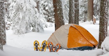 orange and white tent surrounded by snow with snowshoes in front