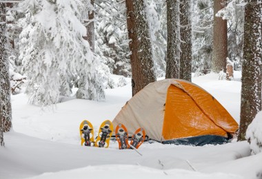 orange and white tent surrounded by snow with snowshoes in front